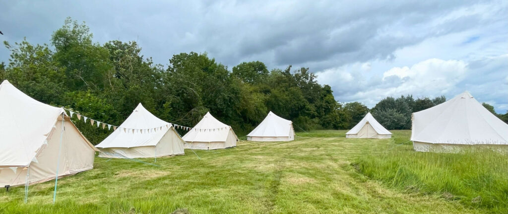 Six bell tents form a wedding glamping village, and await the guests in a freshly mown field