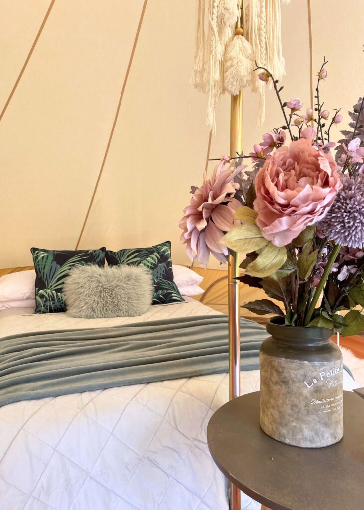 Bell tent interior styled in a colourscheme of duck egg blue and turquoise, with pink and purple flower blooms